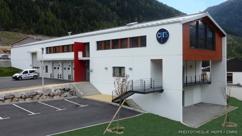 Grand bâtiment blanc avec un logo CNRS, des montagnes en fond