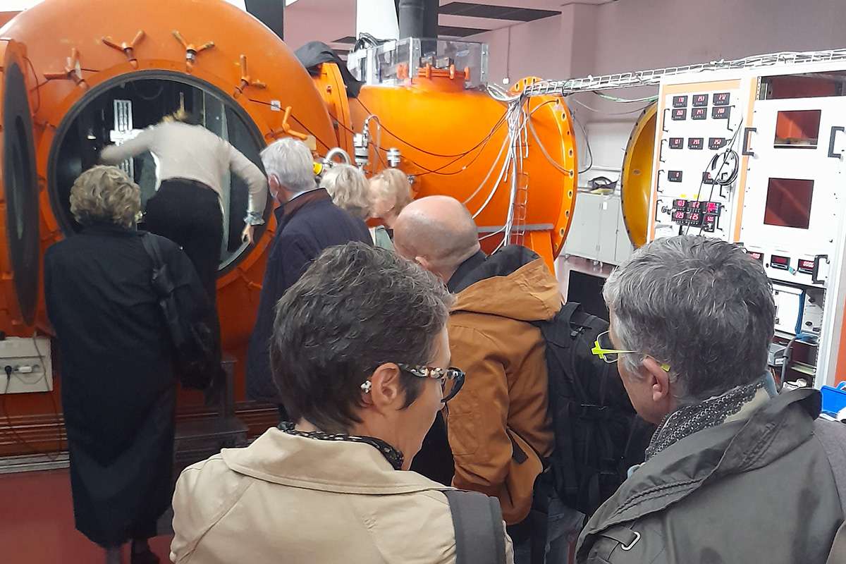 Groupe entrant dans un appareil de test orange, qui ressemble à un mini sous-marin avec des énormes tuyaux qui en partent