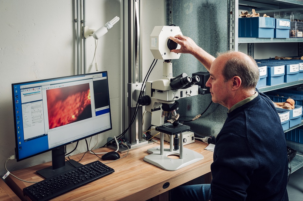 personne manipulant l'instrument (microscope surmonté d'un appareil de spectroscopie) tout en regardant le résultat sur un écran d'ordinateur