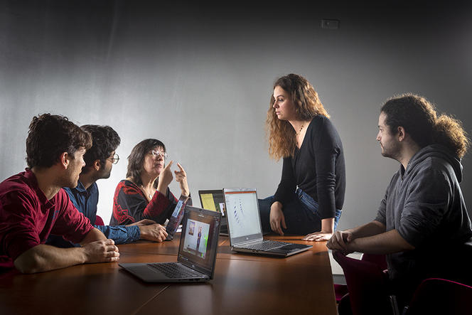 Deux chercheuses et trois chercheurs en discussion autour d'une table remplie d'ordinateurs