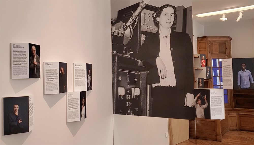 Un des murs du bureau de Jean Perrin rénové dans le cadre de la Maison Poincaré. Sur un mur et un miroir, de nombreux portraits photos de mathématiciens et mathématiciennes (accompagnés de textes explicatifs). En gros sur le miroir, un immense portrait d'Yvette Cauchois debout, en noir et blanc