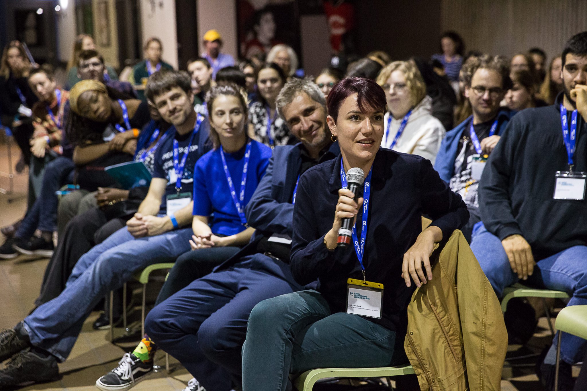 Personnes dans un amphi, la salle est comble, une femme au premier rang tient un micro