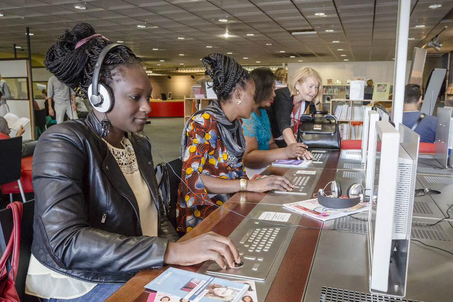 Personnes devant des ordinateurs, avec des revues sur la table et des étagères de livres en fond